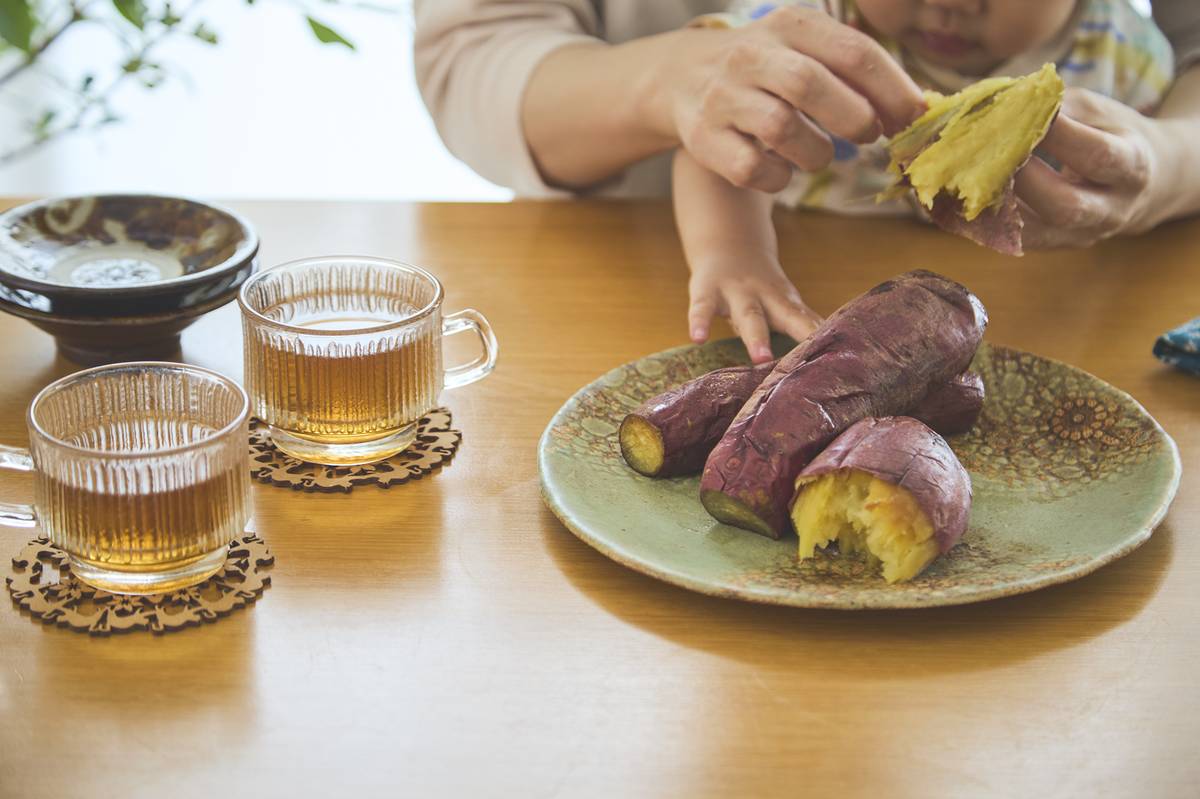 テーブルに盛り付けられた焼き芋に手を伸ばす子供
