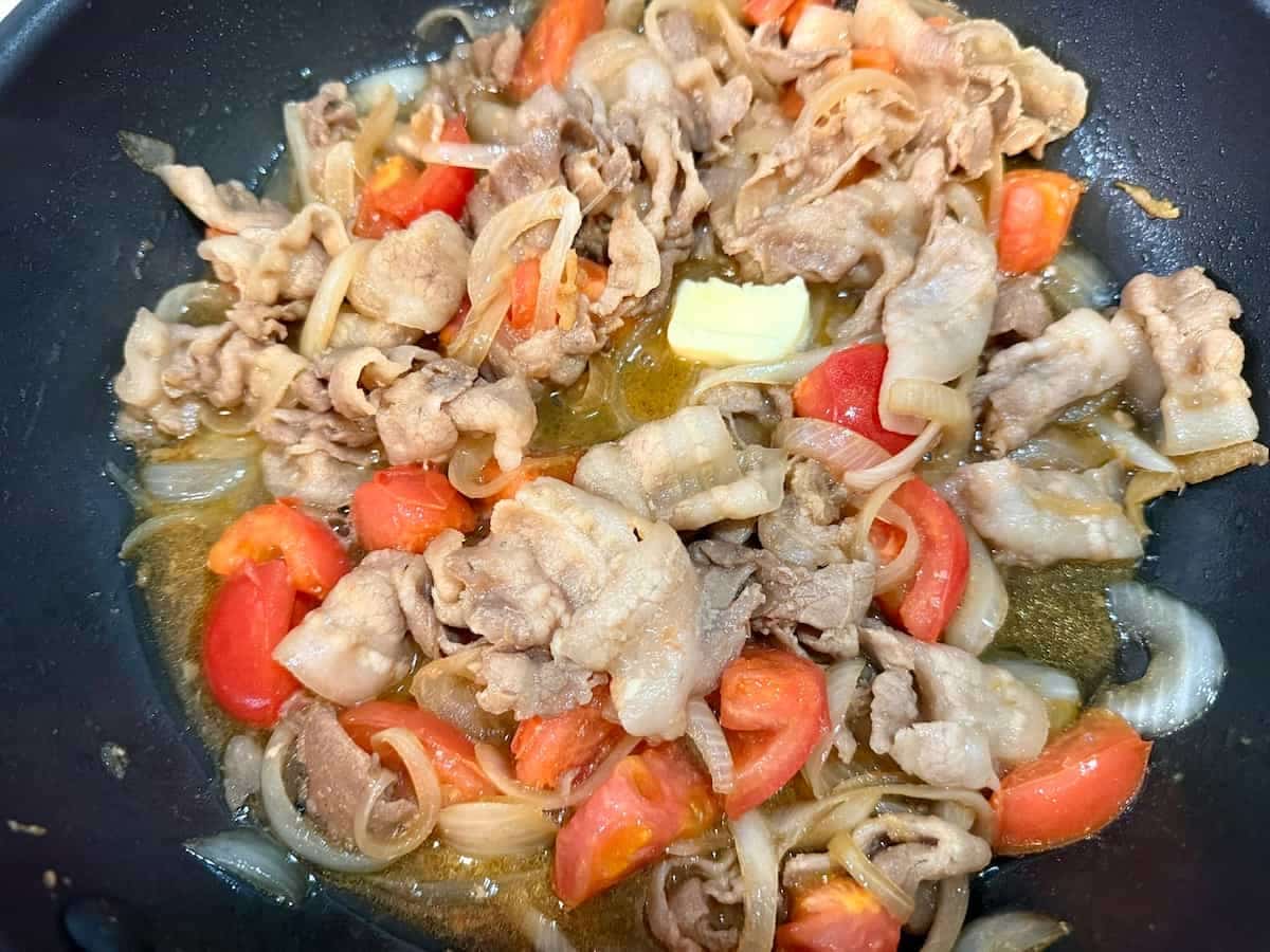 豚肉と玉ねぎをトマトの汁で煮込み、バターを溶かしている様子 トマトバターの洋風しょうが焼き まいのおやつ